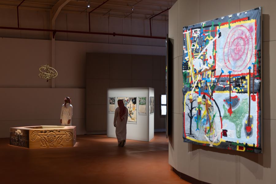 Installation view, gallery hall with carved wood vitrine and textile hanging, JAX District